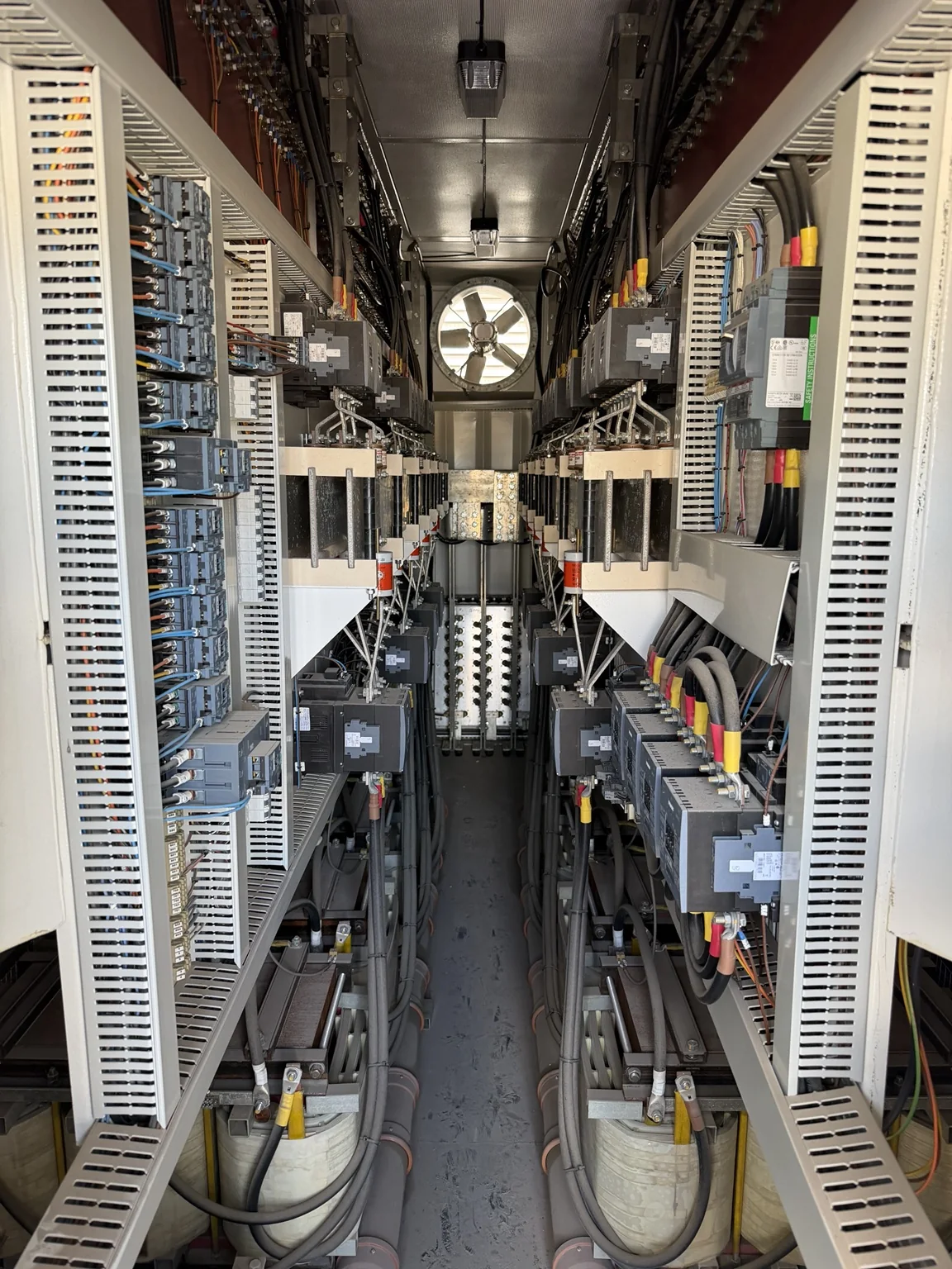 Interior of a commercial load bank showing contactors, bus connections, wiring, and cooling fan